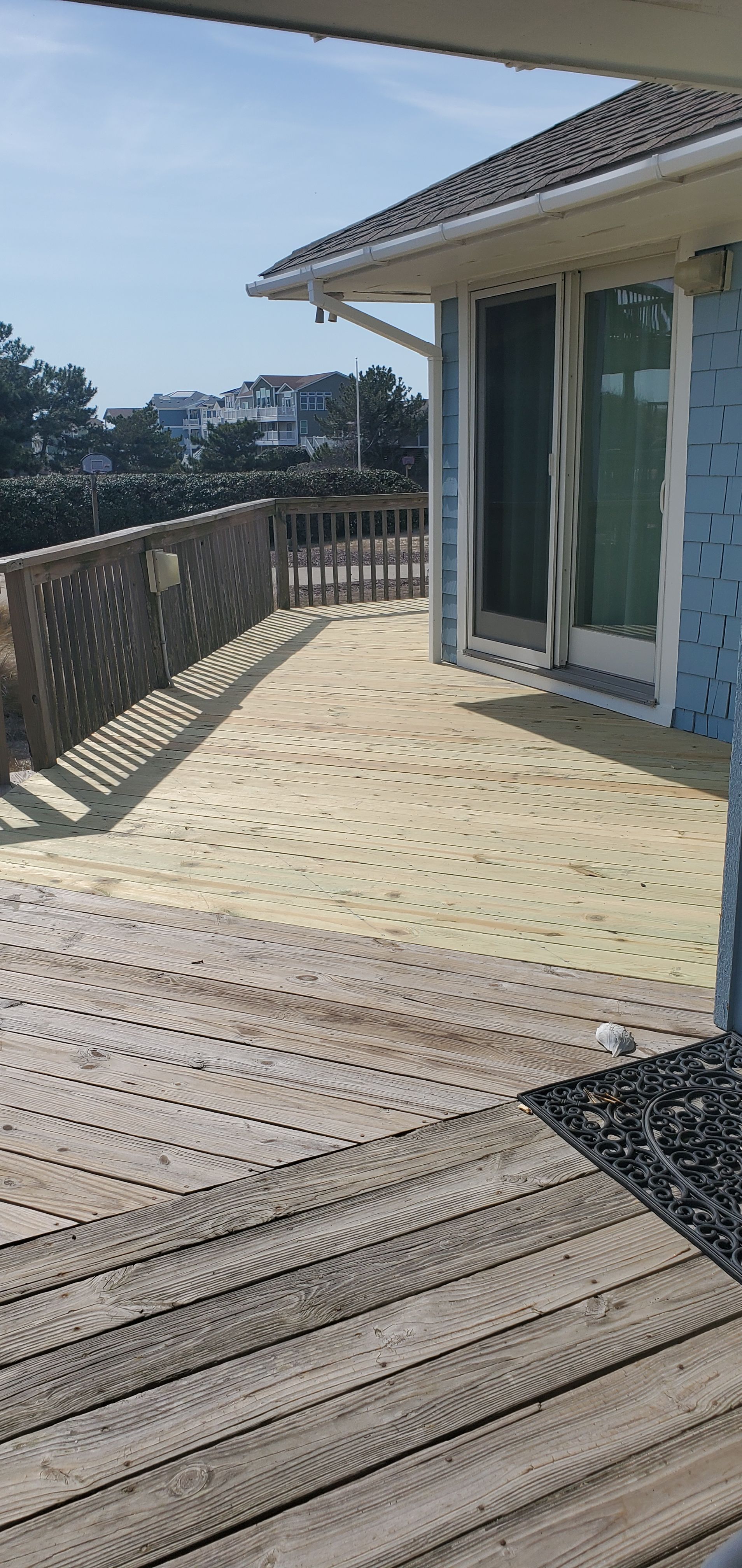 Wooden deck with railing beside a house, overlooking trees and a distant city view on a sunny day