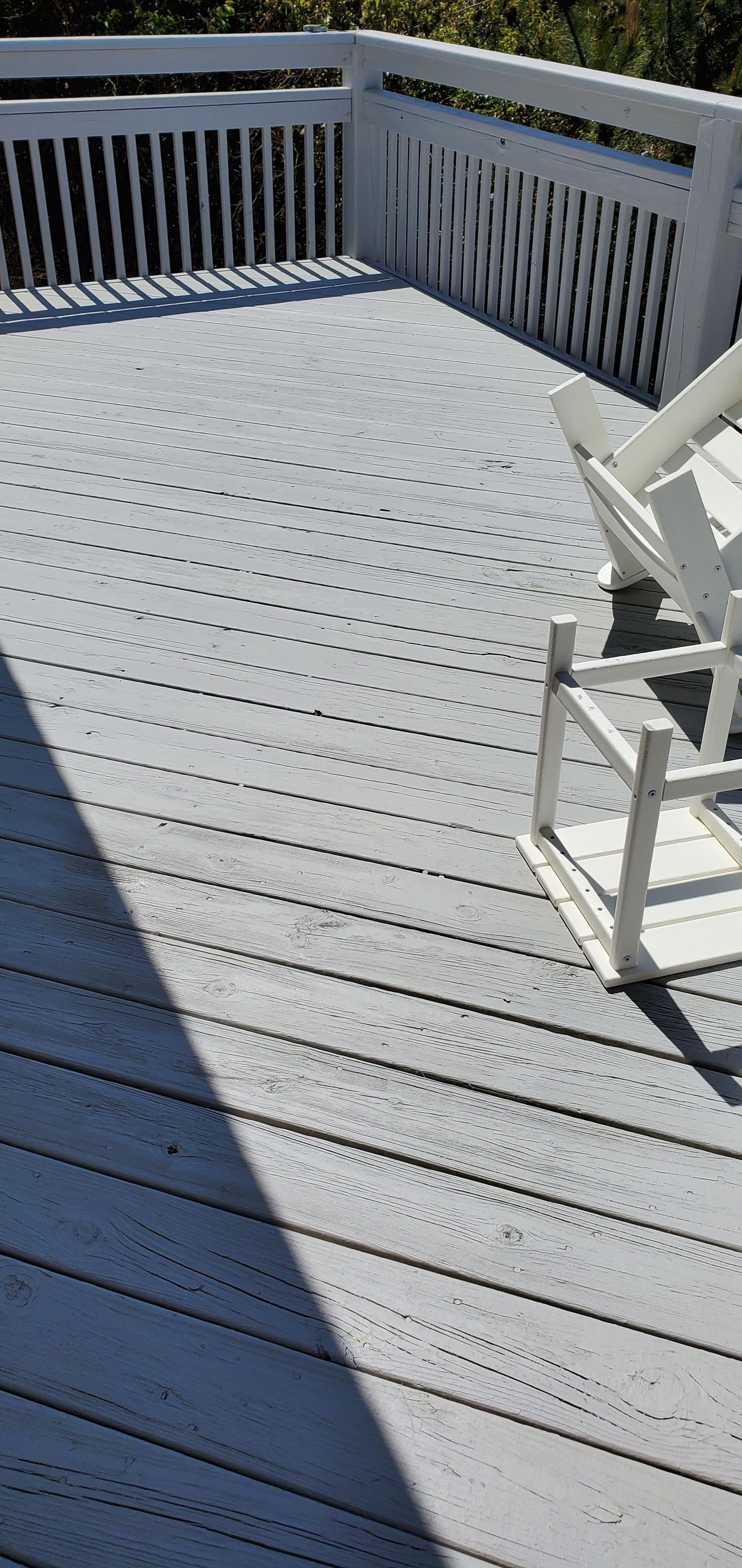 Sunlit gray deck with white railing and stairs, partly shaded by a nearby structure