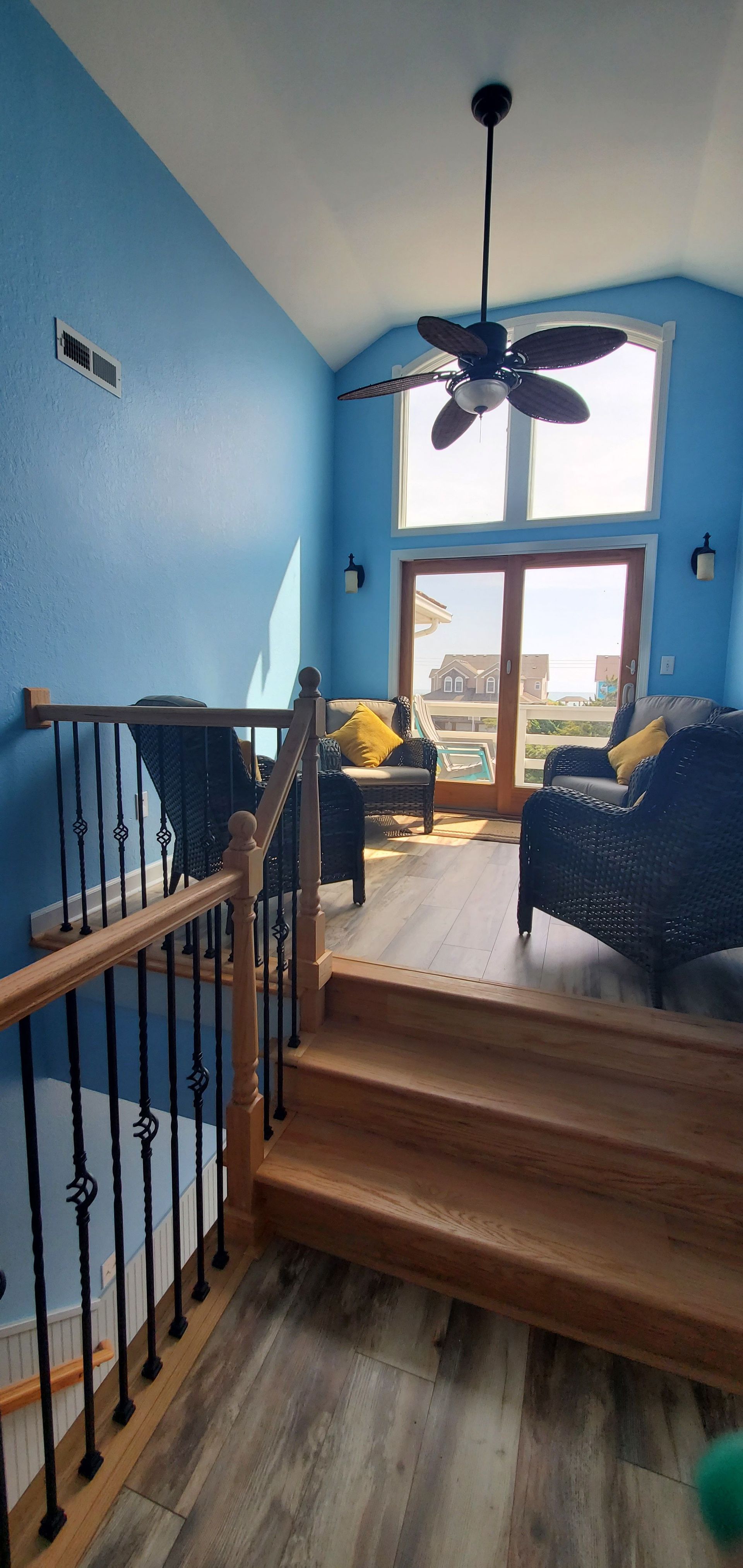 Blue stair landing and living area with wooden steps, high window, ceiling fan, and couch.