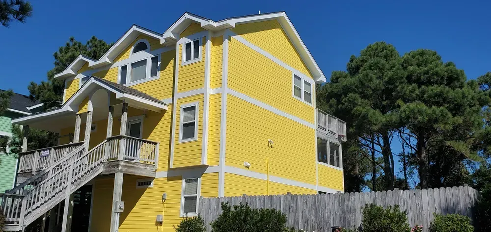 Bright yellow house with white trim on a hillside, viewed from below under a blue sky.