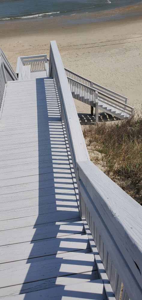 Wooden boardwalk stairs descending to a sandy beach and ocean shoreline