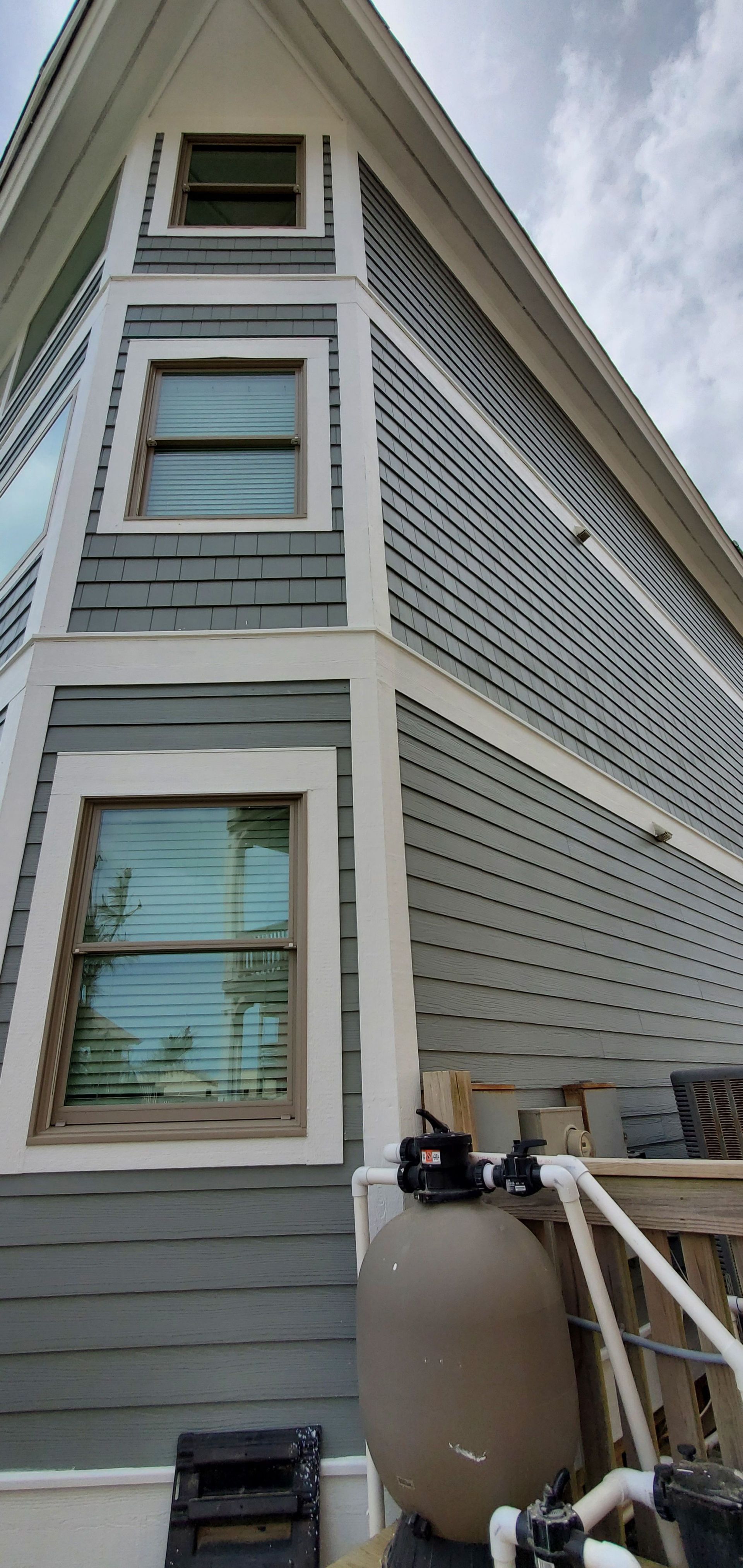 Side view of a gray house with white trim, windows, and an outdoor tank by a small porch staircase