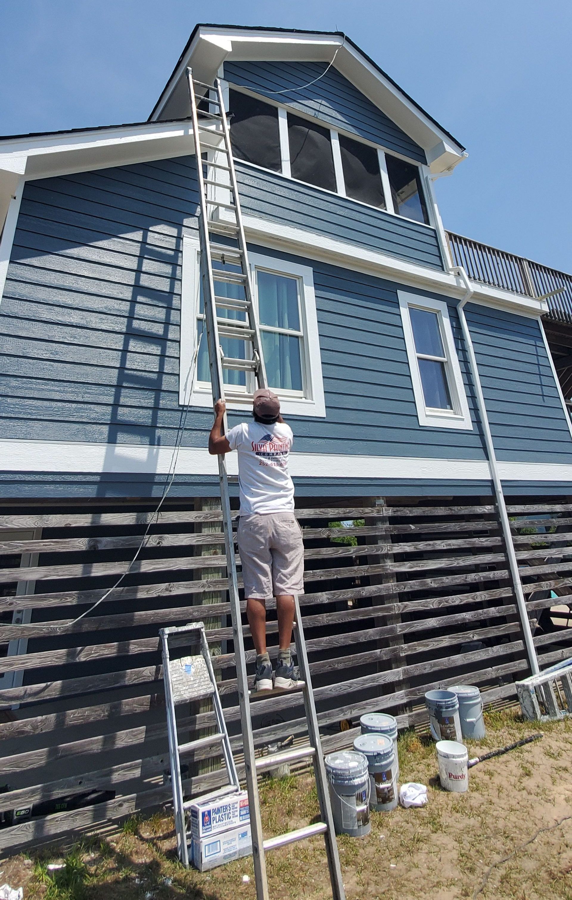Person on ladder painting the exterior of a blue house with white trim