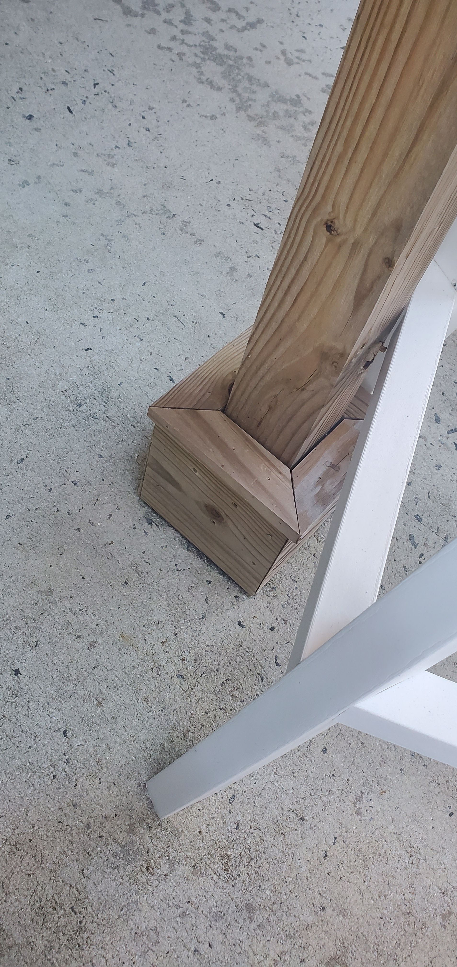 Close-up of a wooden post base anchored to a speckled concrete floor beside a white chair leg.
