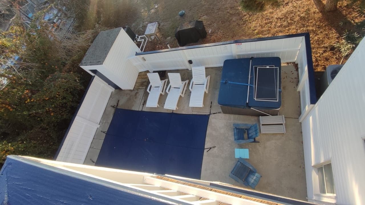 Aerial view of a small backyard patio with lounge chairs, a blue pool cover, and surrounding walls.