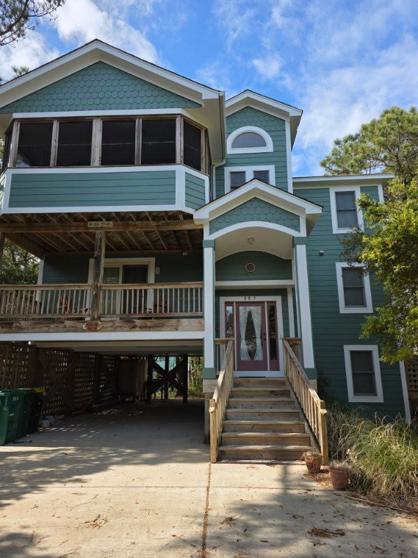 Blue beach house on stilts with wraparound porches and front stairs under a partly cloudy sky