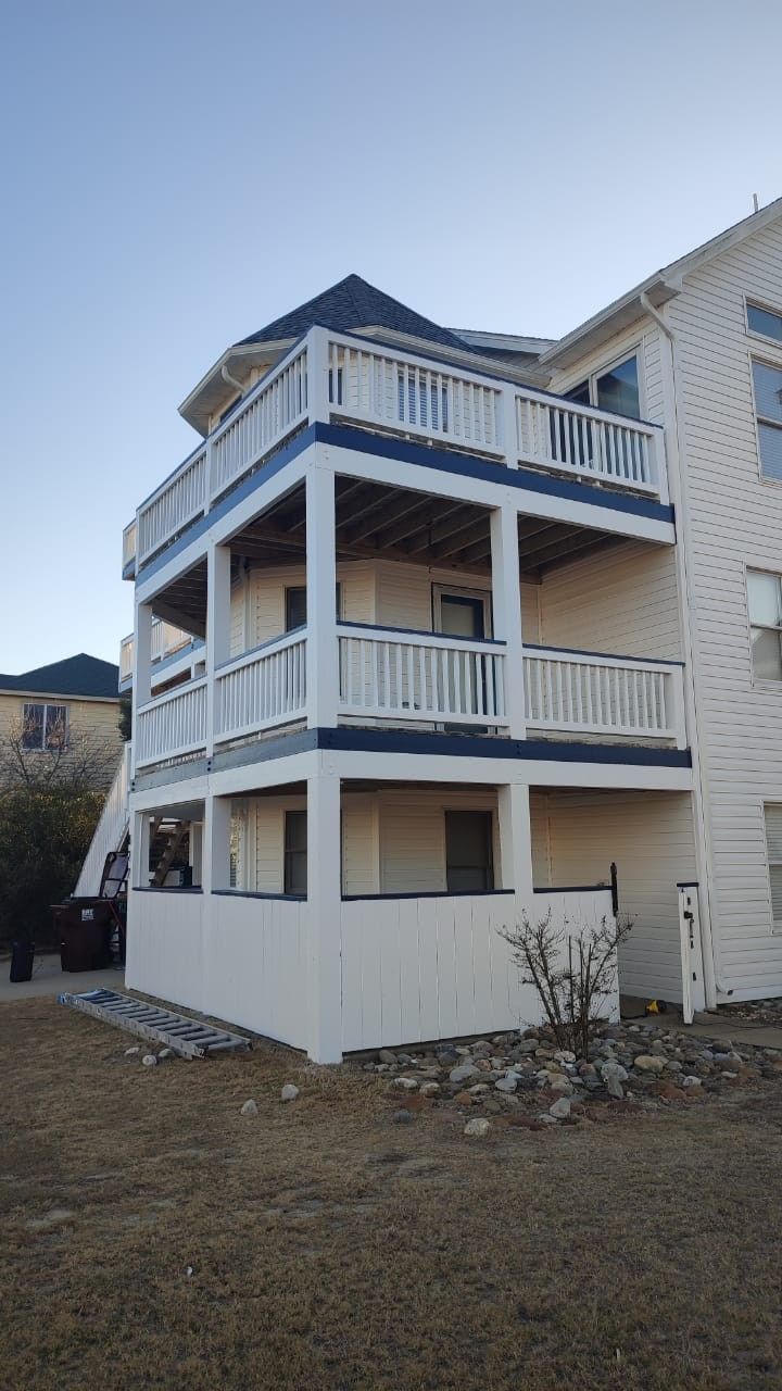 Three-story white house with blue trim and wraparound balconies on a grassy lot
