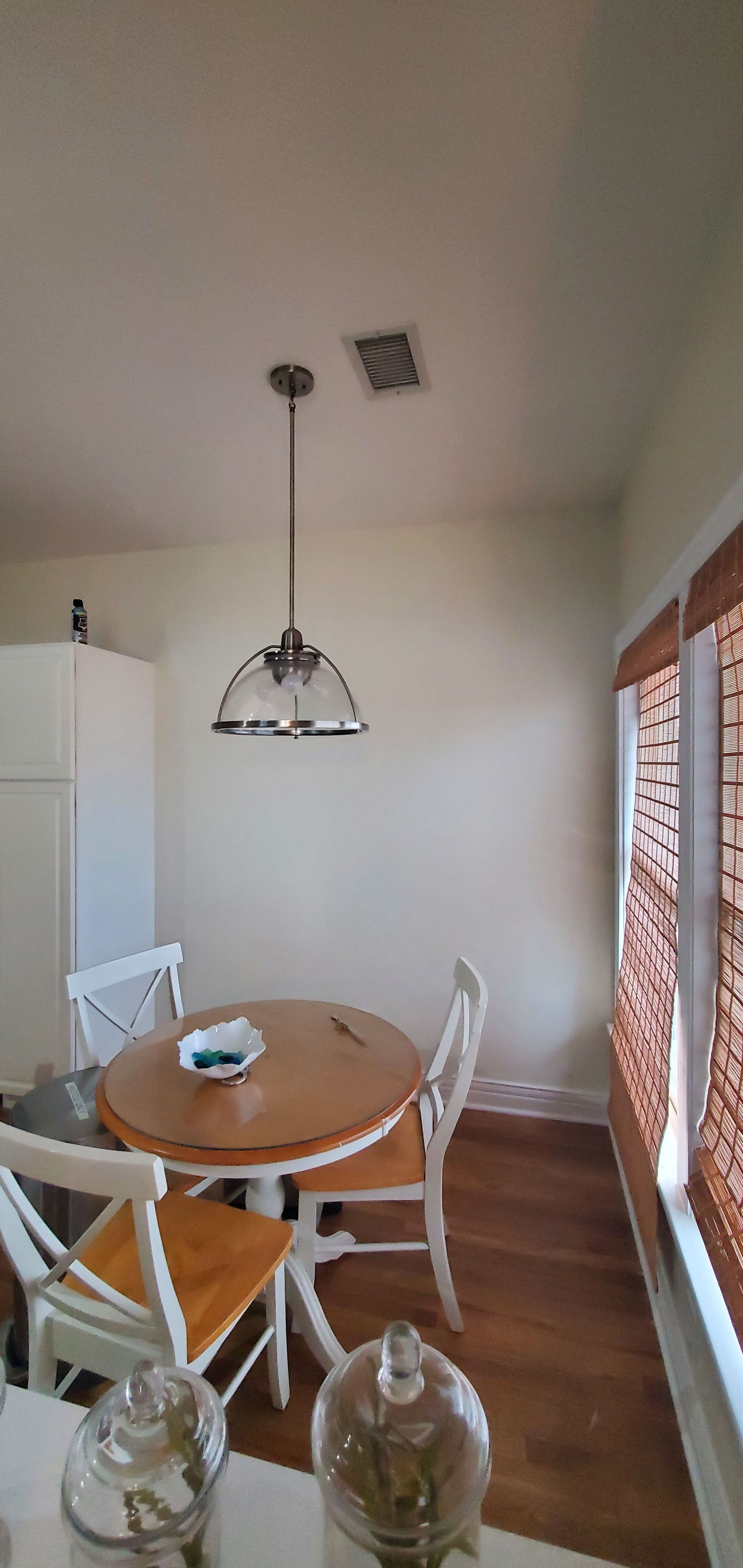 Bright dining nook with round wooden table, white chairs, hanging light, and sliding glass doors.
