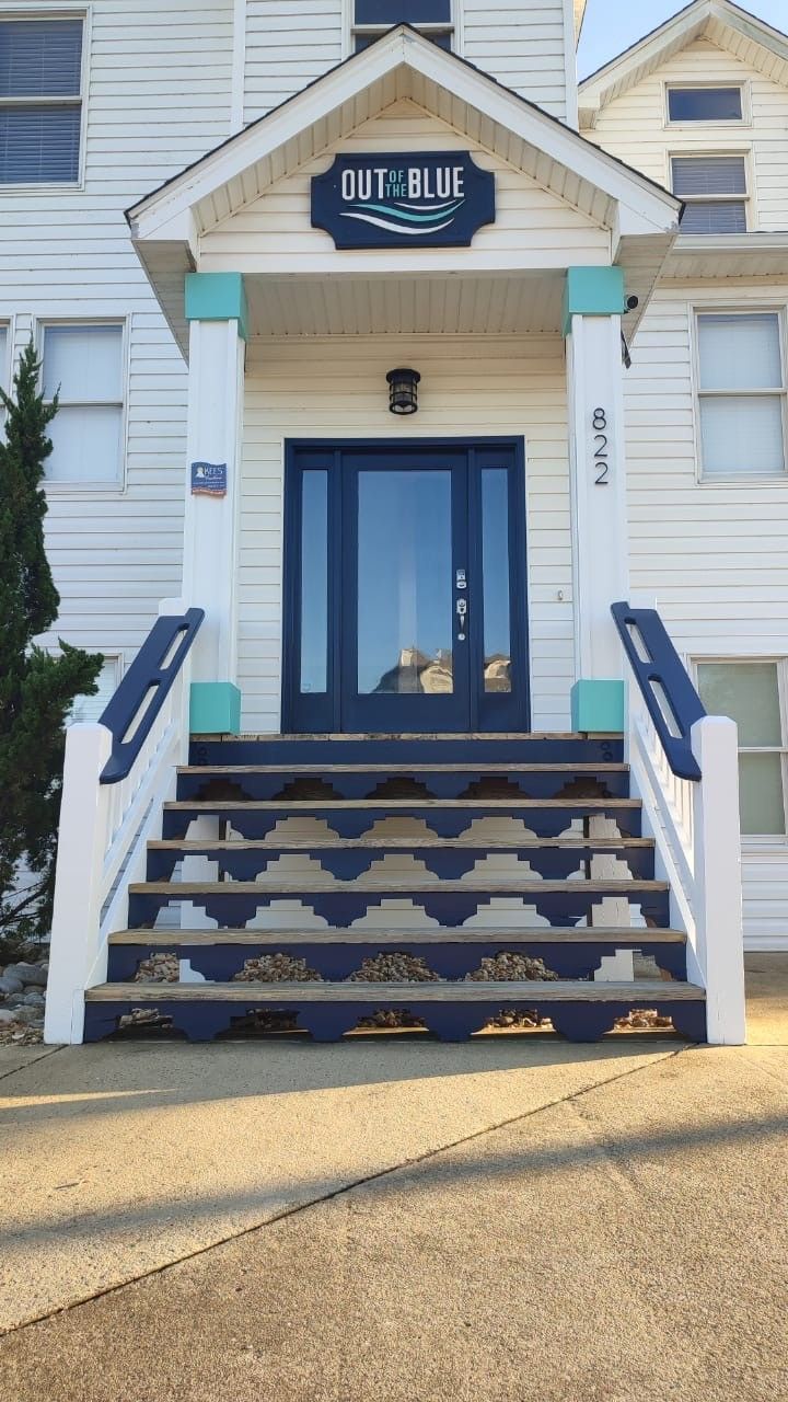 Building entrance with blue double doors, steps, and a hanging sign above the porch.