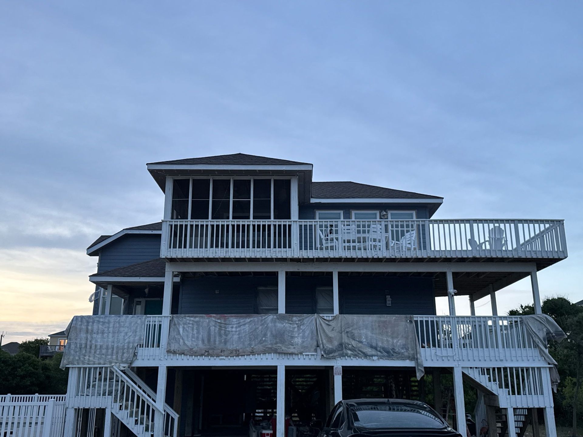 Two-story gray beach house with white railings and stairs under a cloudy sky
