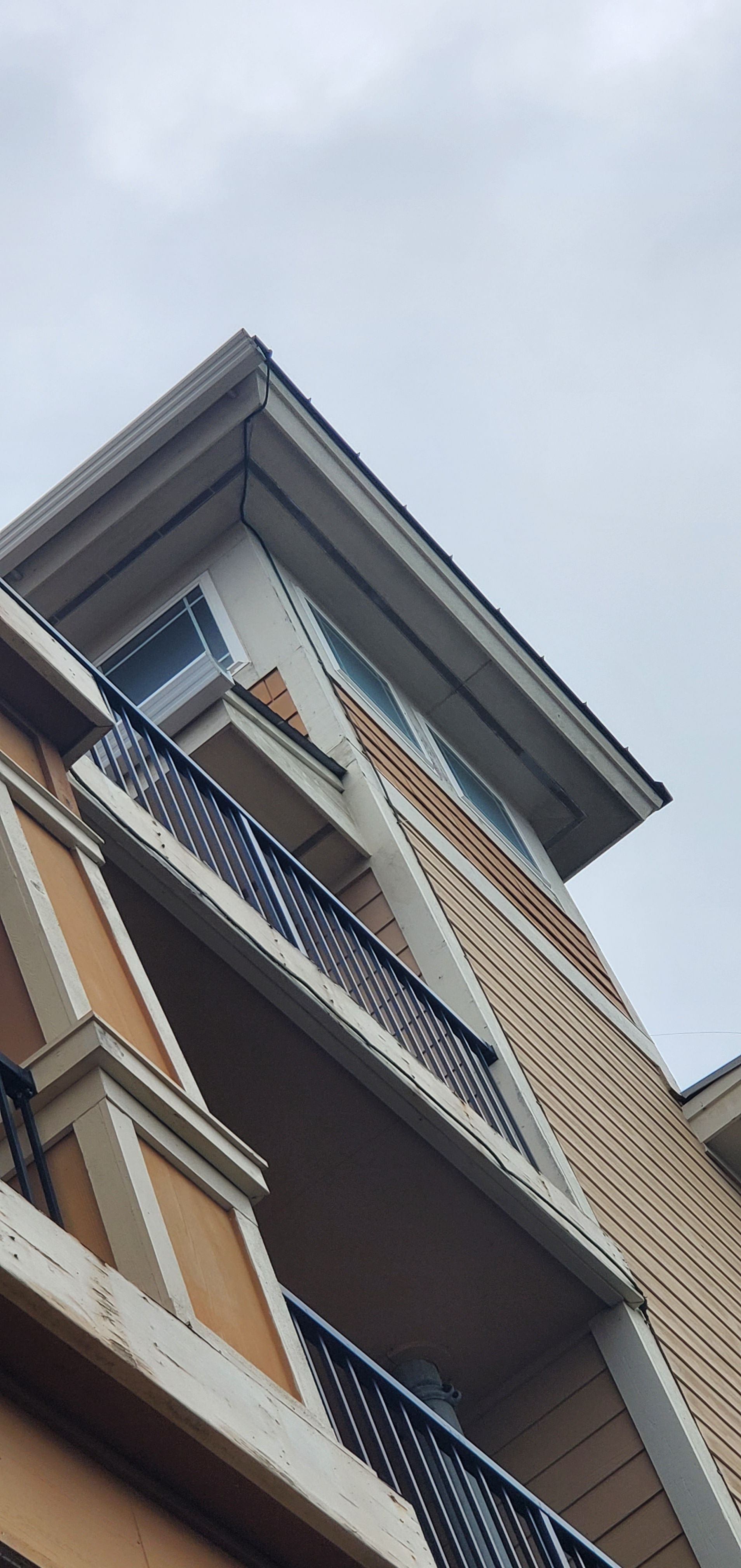 Upward view of a modern apartment building with balconies and a slanted roof against a cloudy sky