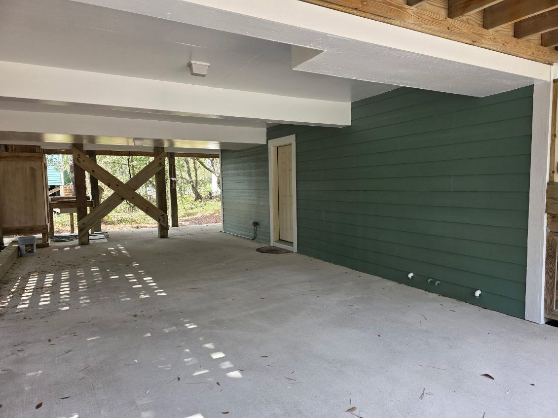 Empty covered patio with concrete floor, green siding, exposed beams, and open view to the yard.