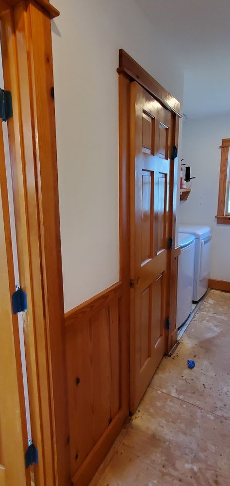 Narrow hallway with wooden wainscoting, a closed wood door, and a laundry room visible at the end.