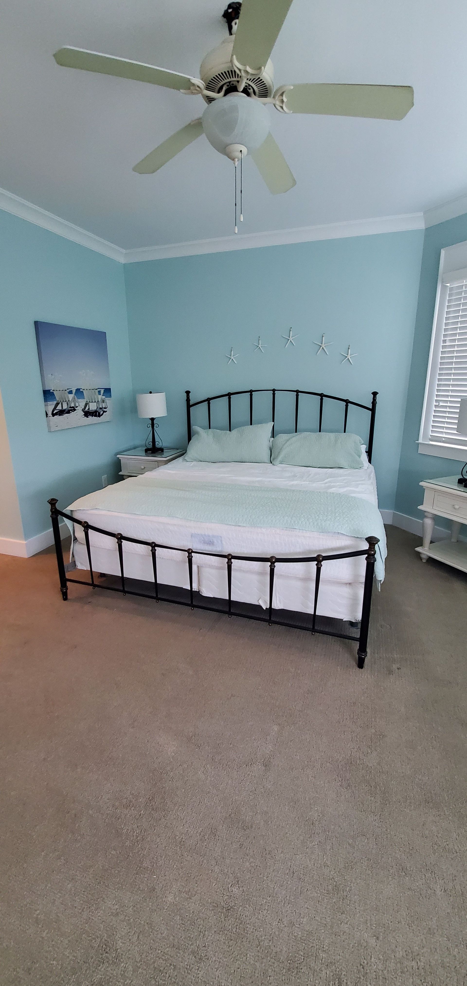Light blue bedroom with a metal bed, white bedding, ceiling fan, and carpet.