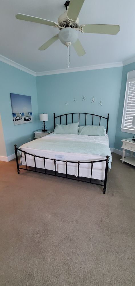 Light blue bedroom with a black metal bed, white bedding, ceiling fan, and beige carpet