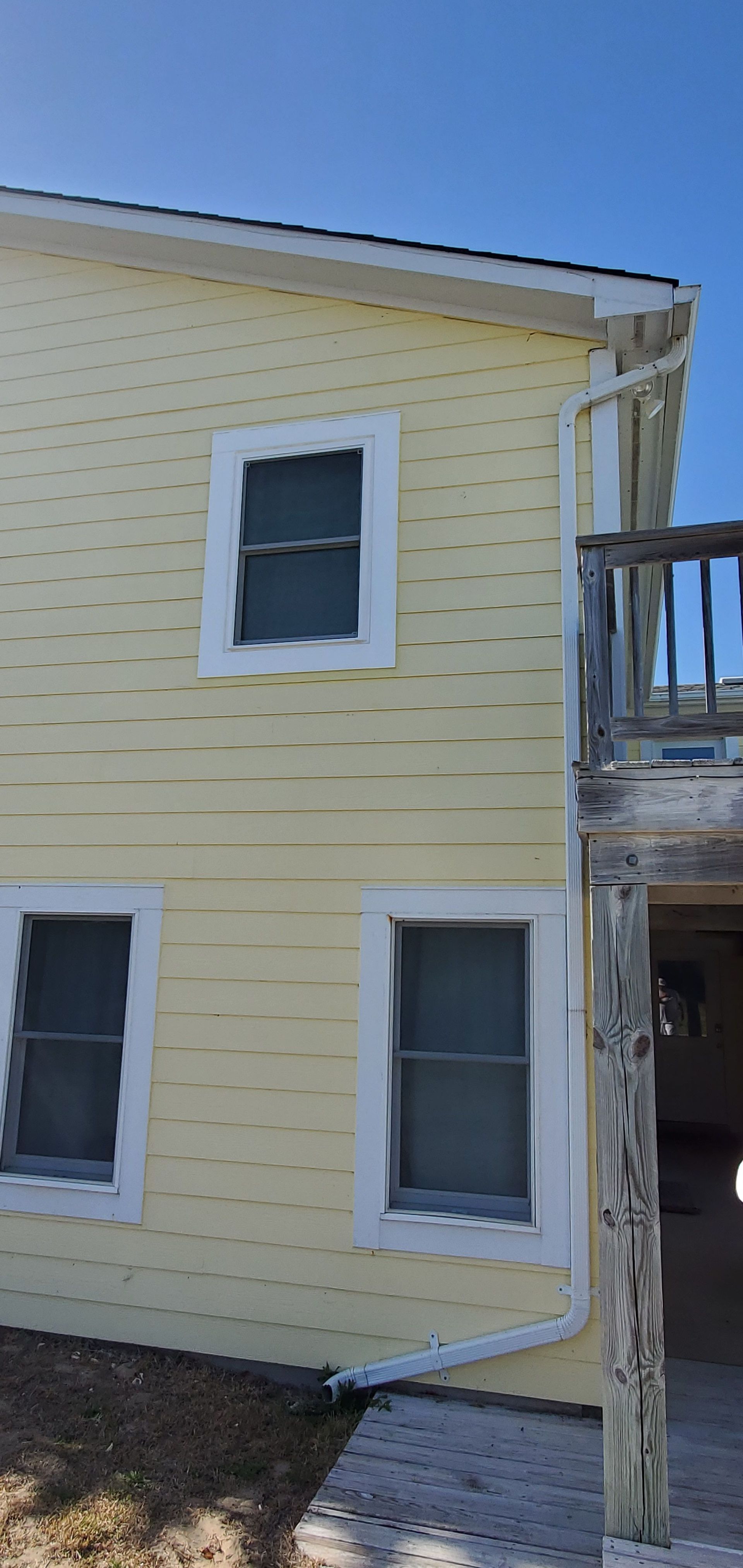 Yellow house exterior with white-trim windows and a wooden post in the foreground