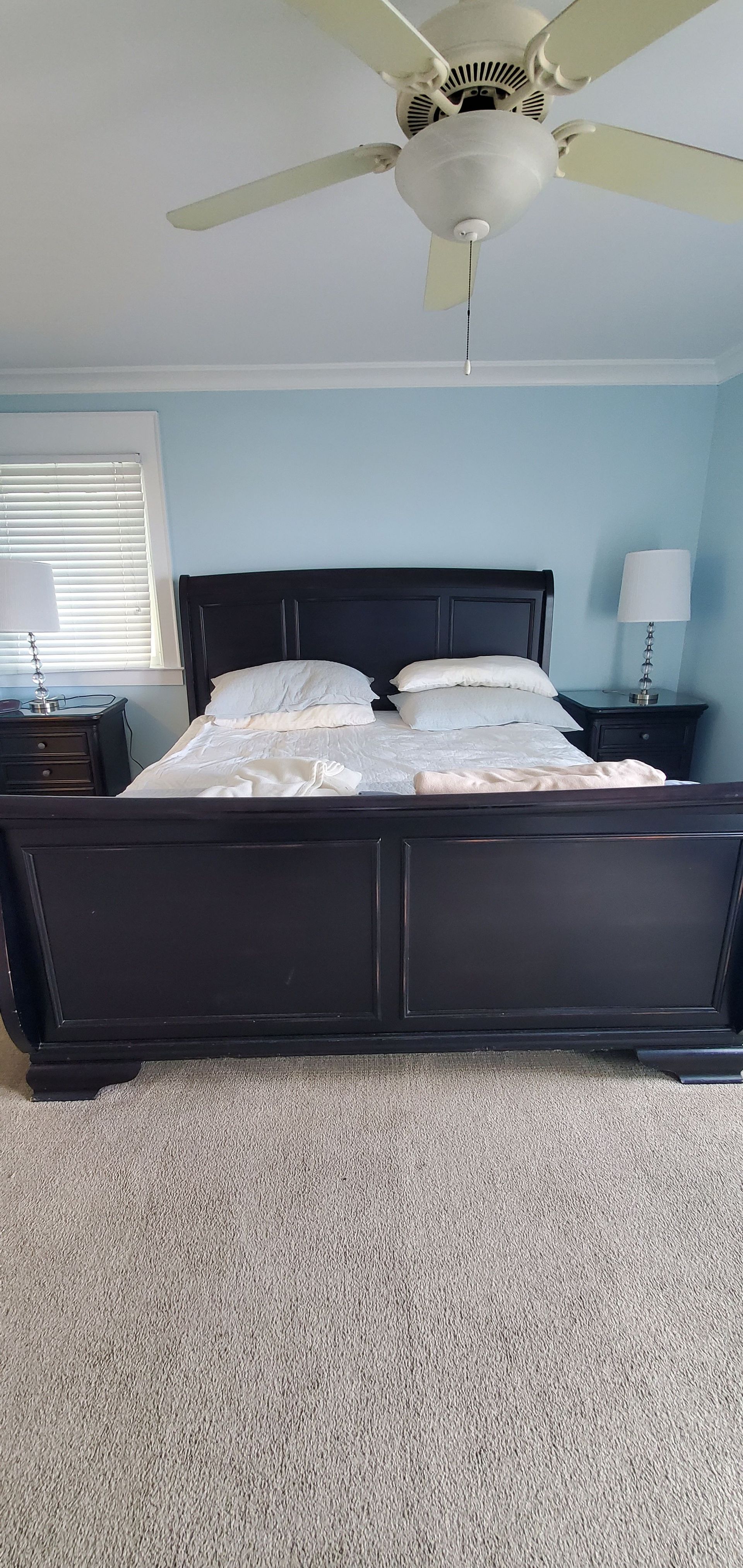 Bedroom with a dark wood bed, white bedding, gray walls, ceiling fan, and speckled carpet.