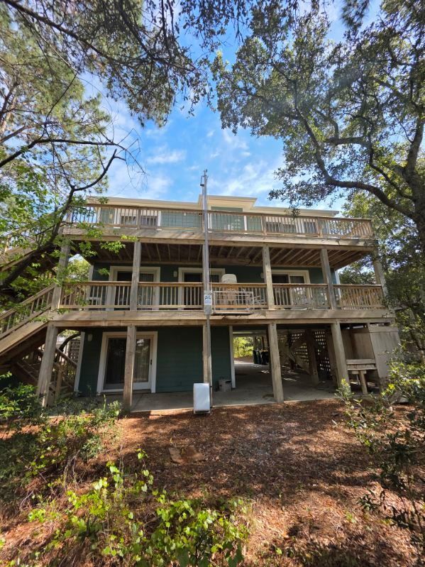 Two-story wooden house with wraparound porches, surrounded by trees and leaf-covered ground