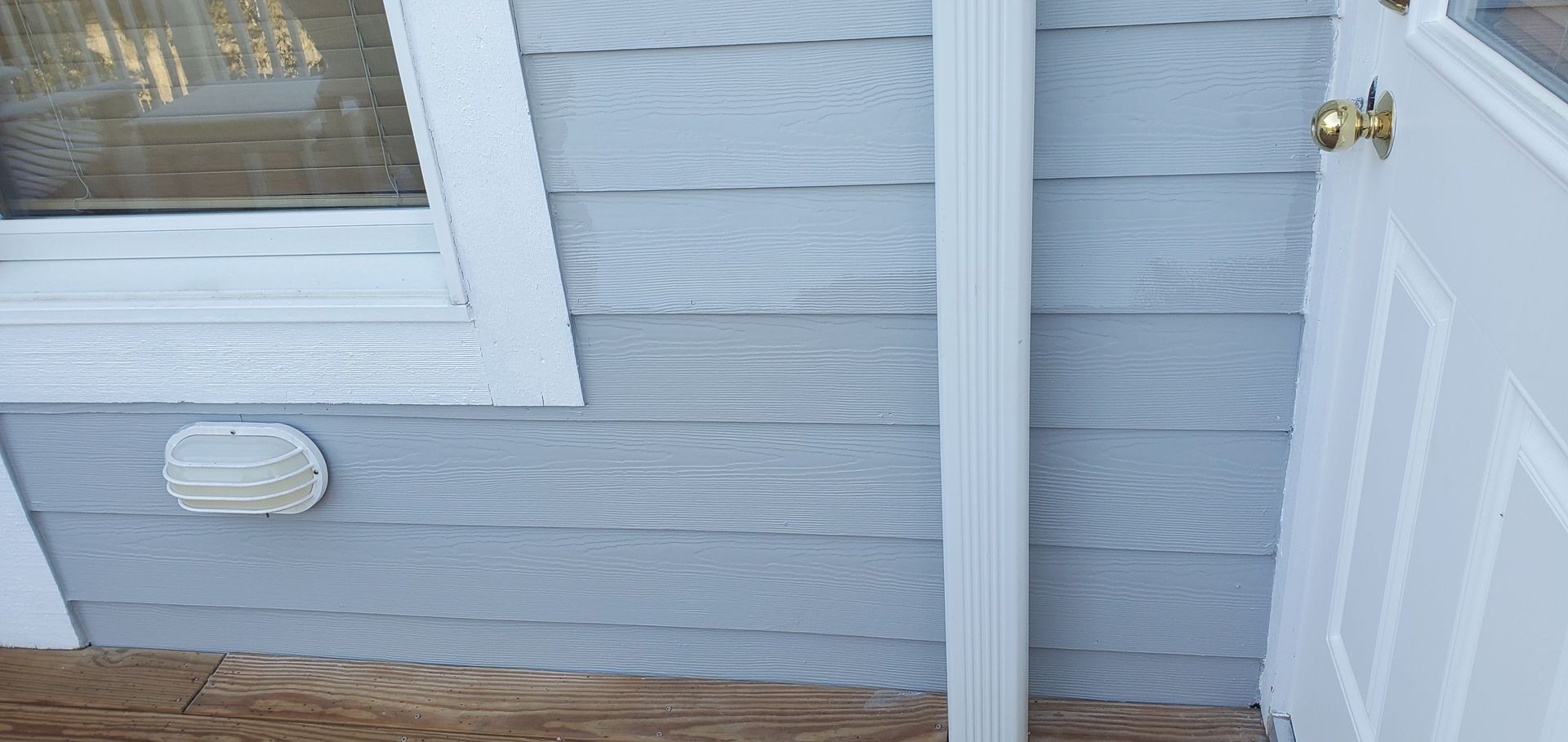 Gray house siding with a window, outdoor light, and a white door on a porch.