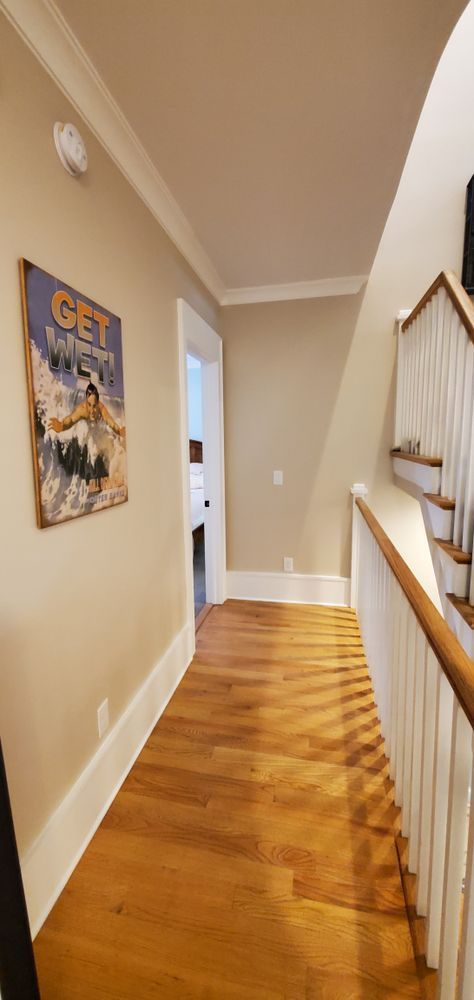 Hallway with hardwood floor, beige walls, and a stair railing on the right