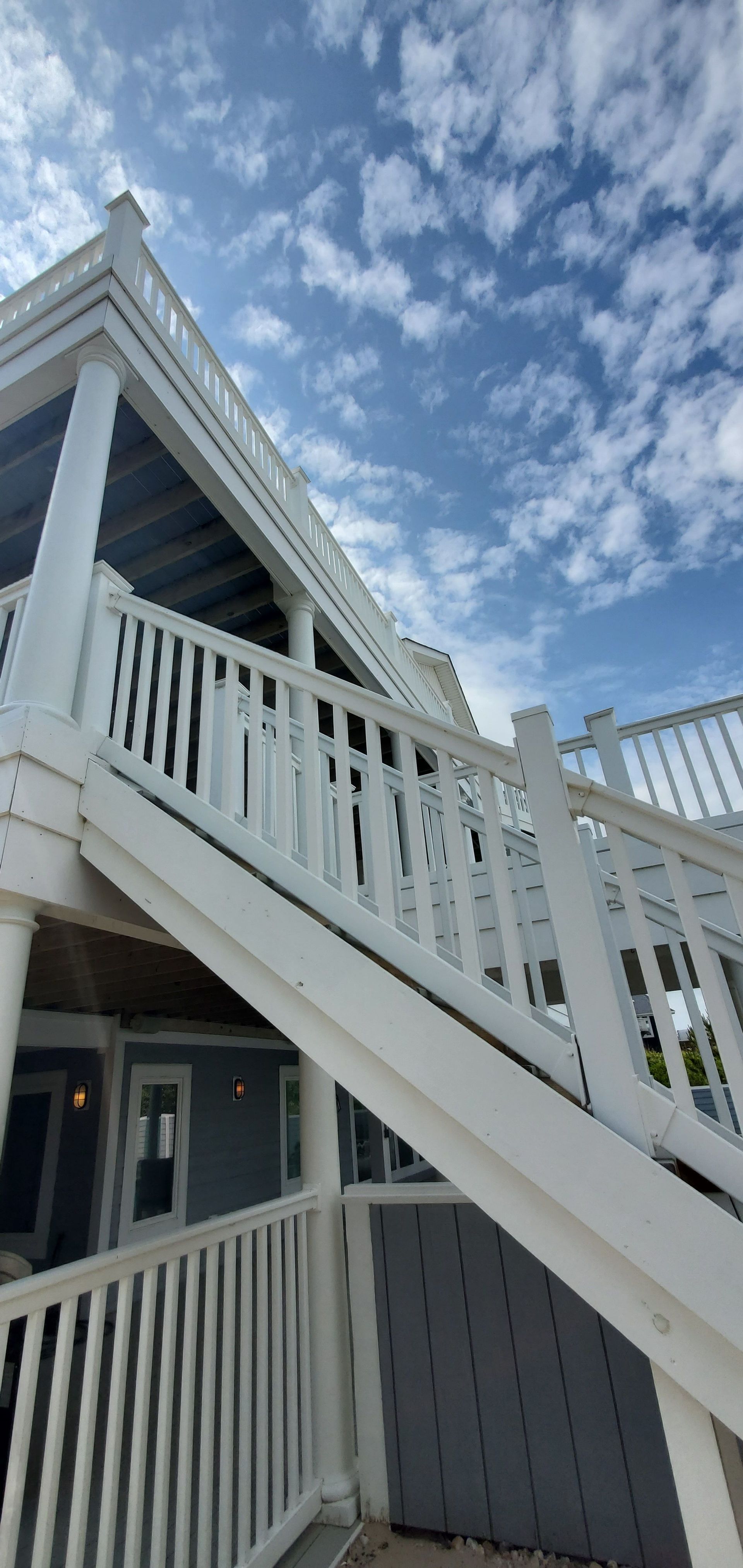 White staircase and balcony of a house under a blue, partly cloudy sky