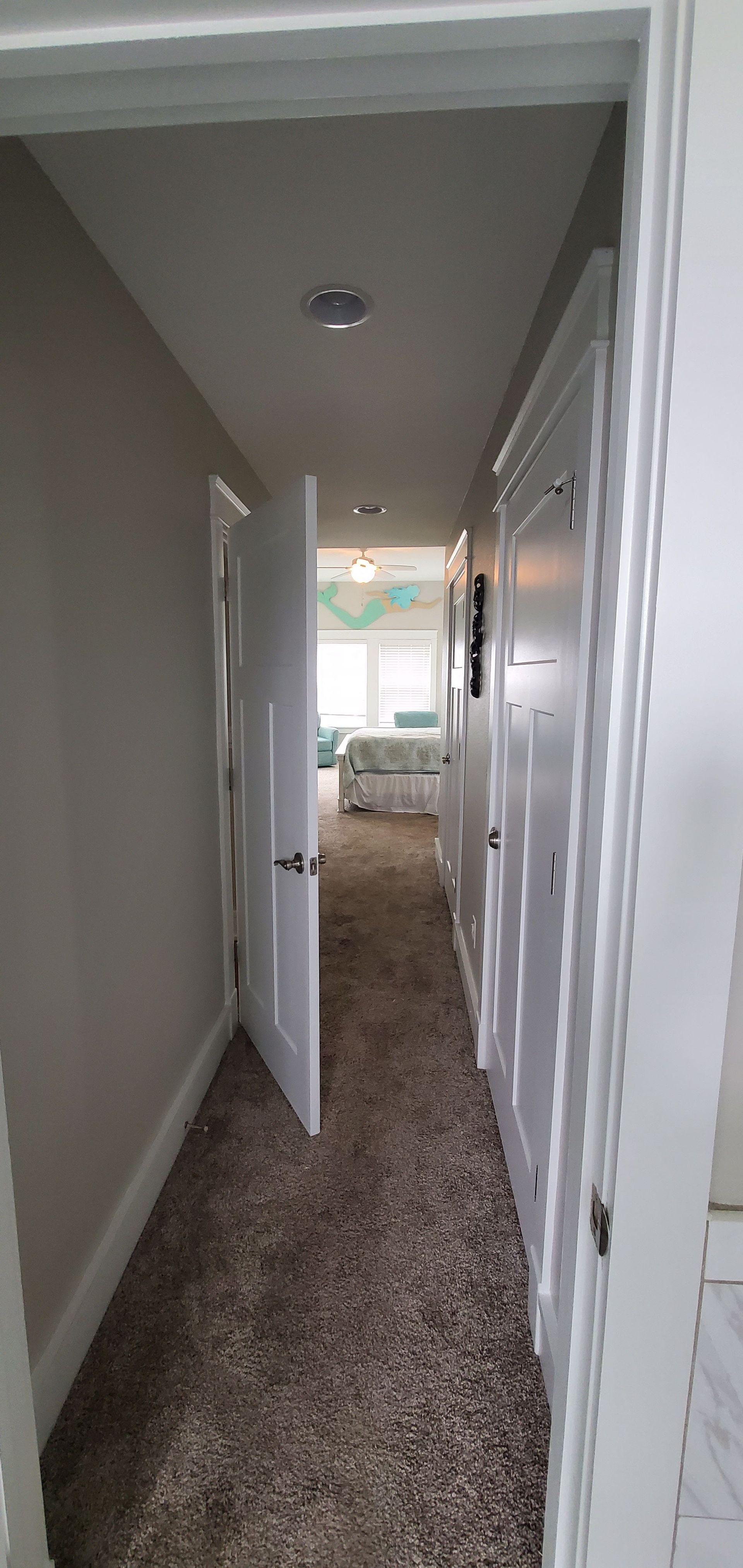 Narrow carpeted hallway with open doors leading to a bright room at the end.