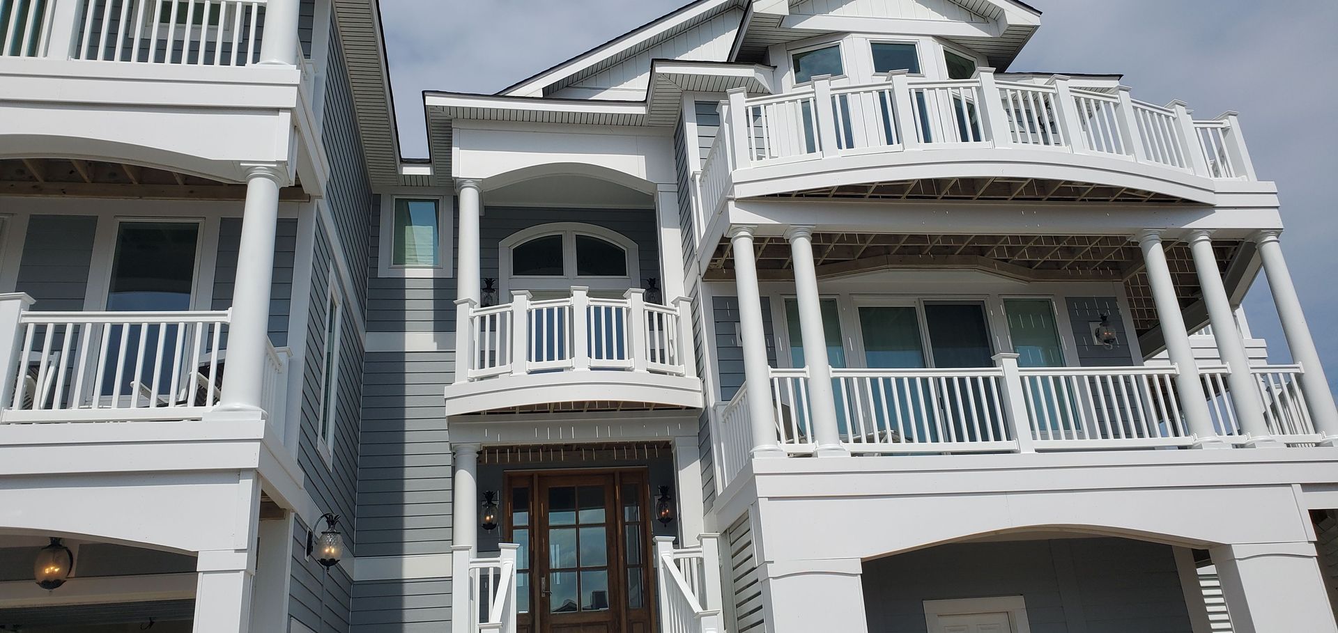 White multi-story house with balconies and white railings under a bright sky
