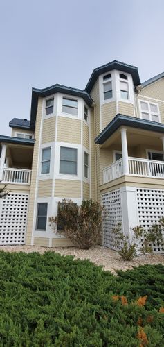Multi-story beige apartment building with white balconies and hedges in front