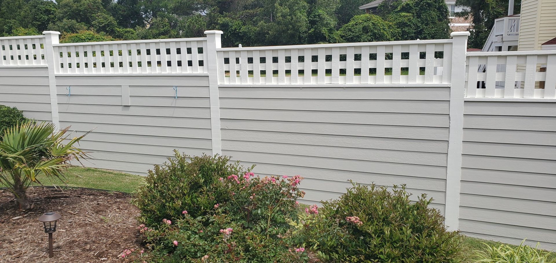 White vinyl privacy fence behind a garden with shrubs and pink flowers