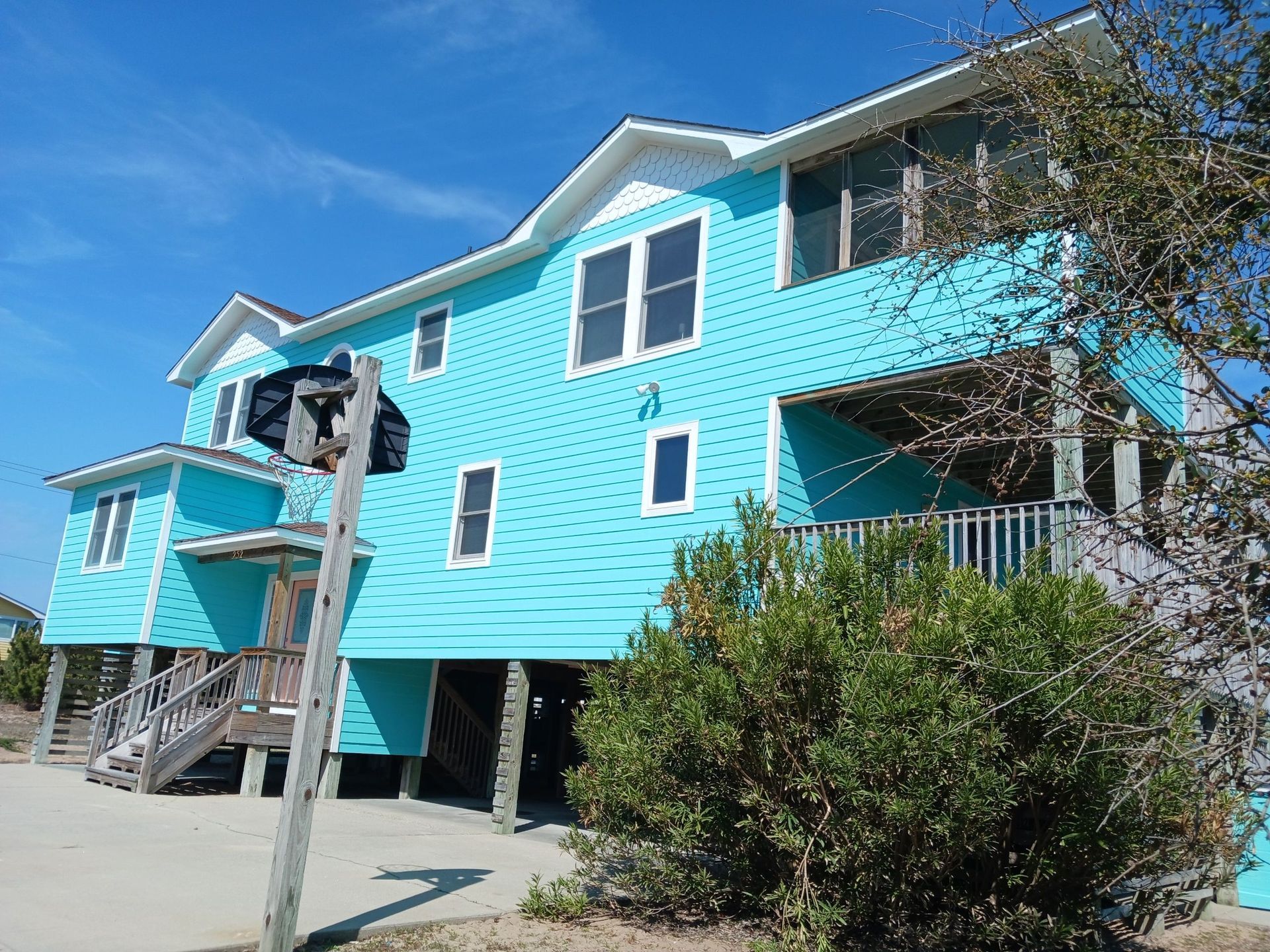 Bright turquoise beach house on stilts with stairs and balconies, seen on a sunny day