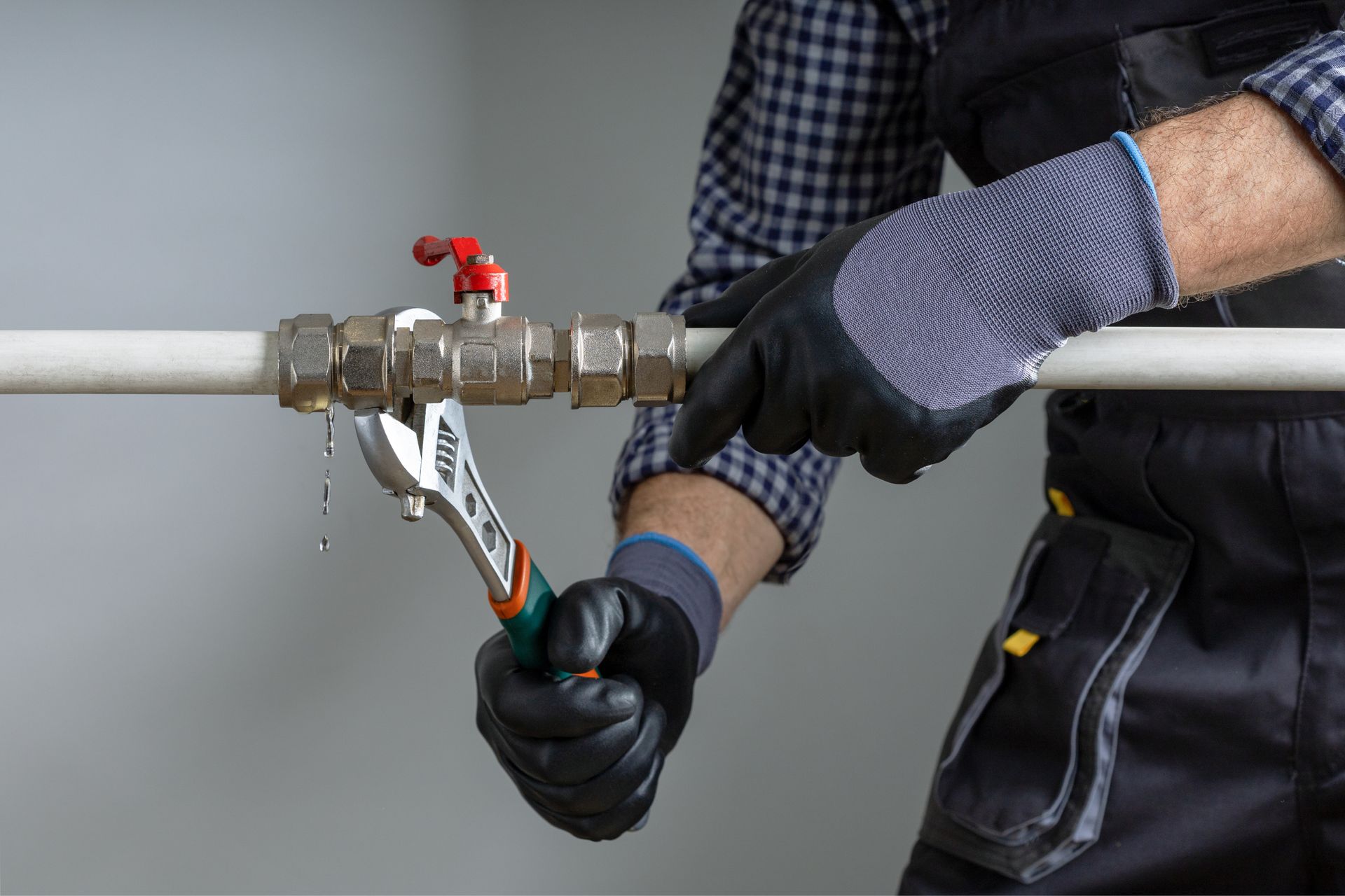 Worker using a wrench to tighten a valve on a white pipe, wearing black gloves and a plaid shirt.