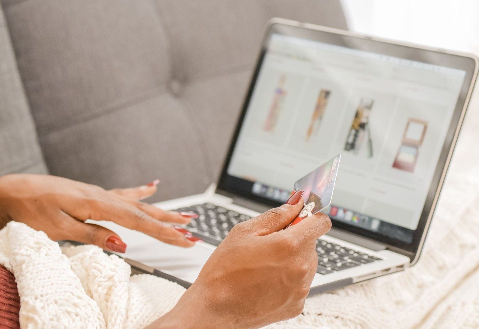 A woman is holding a credit card in front of a laptop computer.