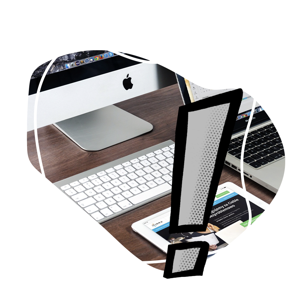A computer , keyboard , tablet , and laptop on a desk with an exclamation point.