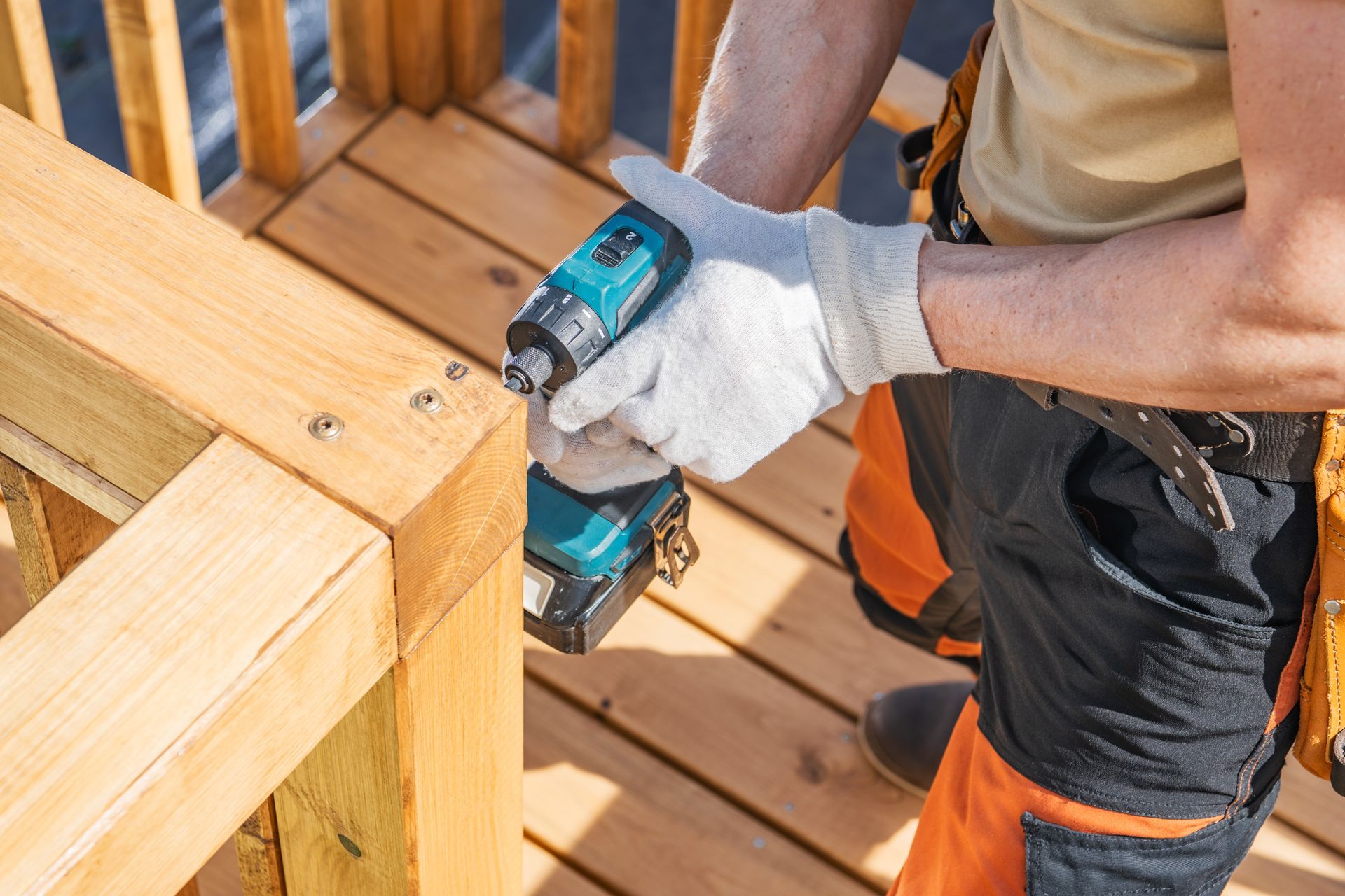 Gloved hands use a cordless drill to fasten a wooden deck railing.