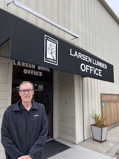 Man standing in front of the Larsen Lumber Office with a black awning and sign.