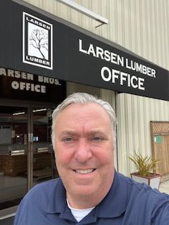 Man in blue shirt smiles in front of a Larsen Lumber office building.