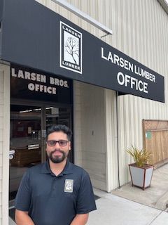 Man stands in front of Larsen Lumber Office. Black awning over door, sign with logo.