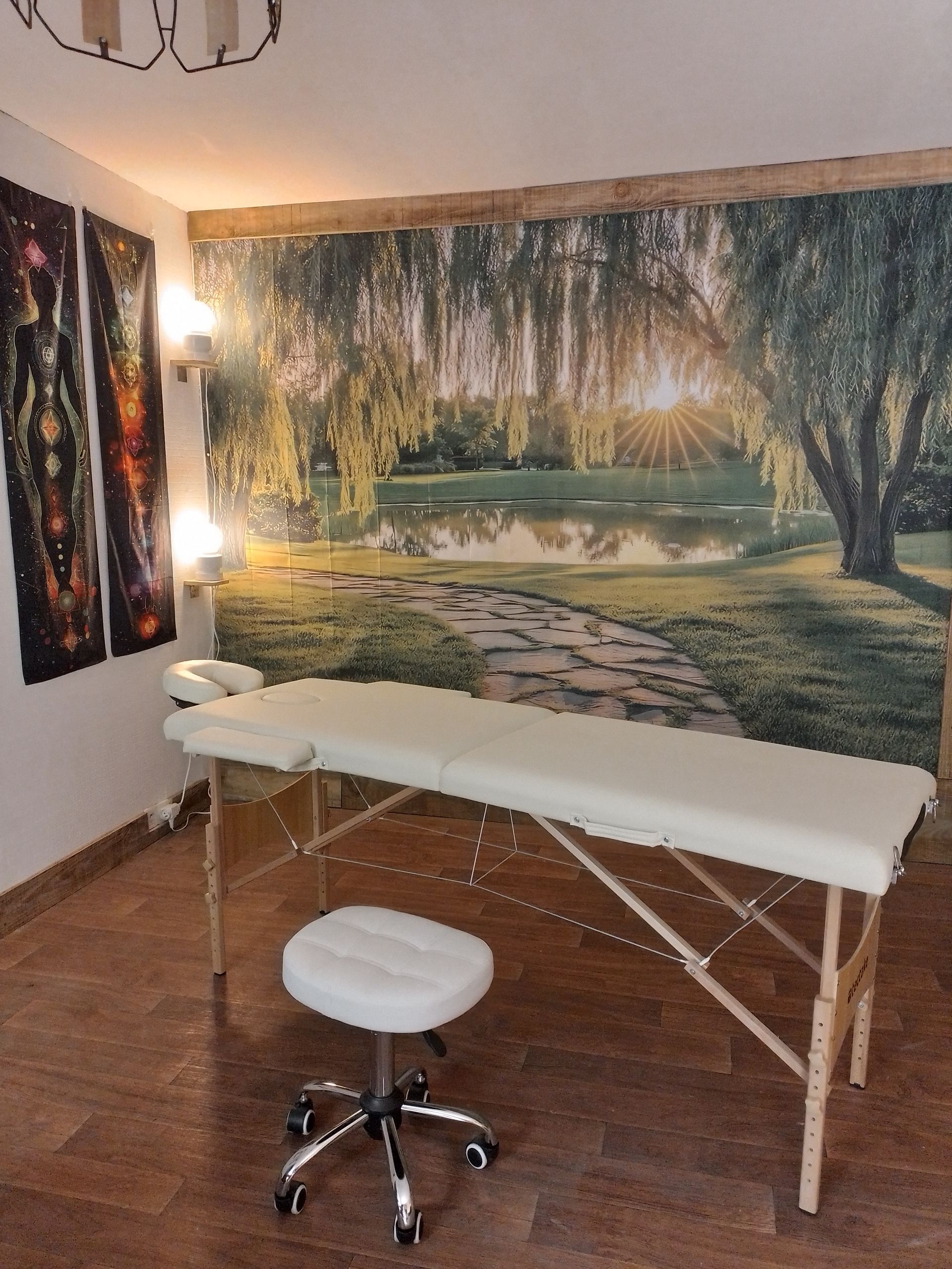 Table de massage et tabouret dans une pièce décorée d'une fresque représentant la nature et baignée d'une lumière chaleureuse