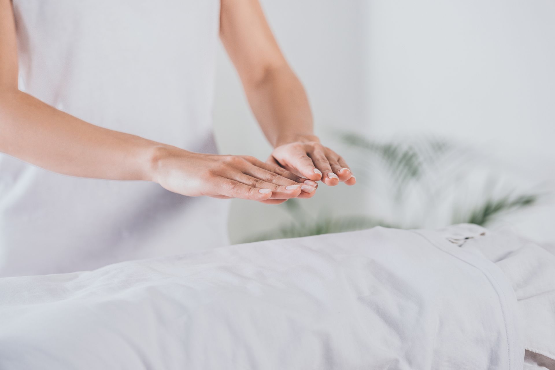 Des mains effectuent un massage sur une personne allongée sous une couverture blanche dans une salle de spa lumineuse.