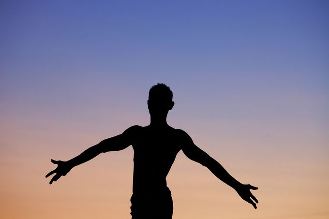 Silhouette d'une personne les bras tendus sur un ciel de coucher de soleil