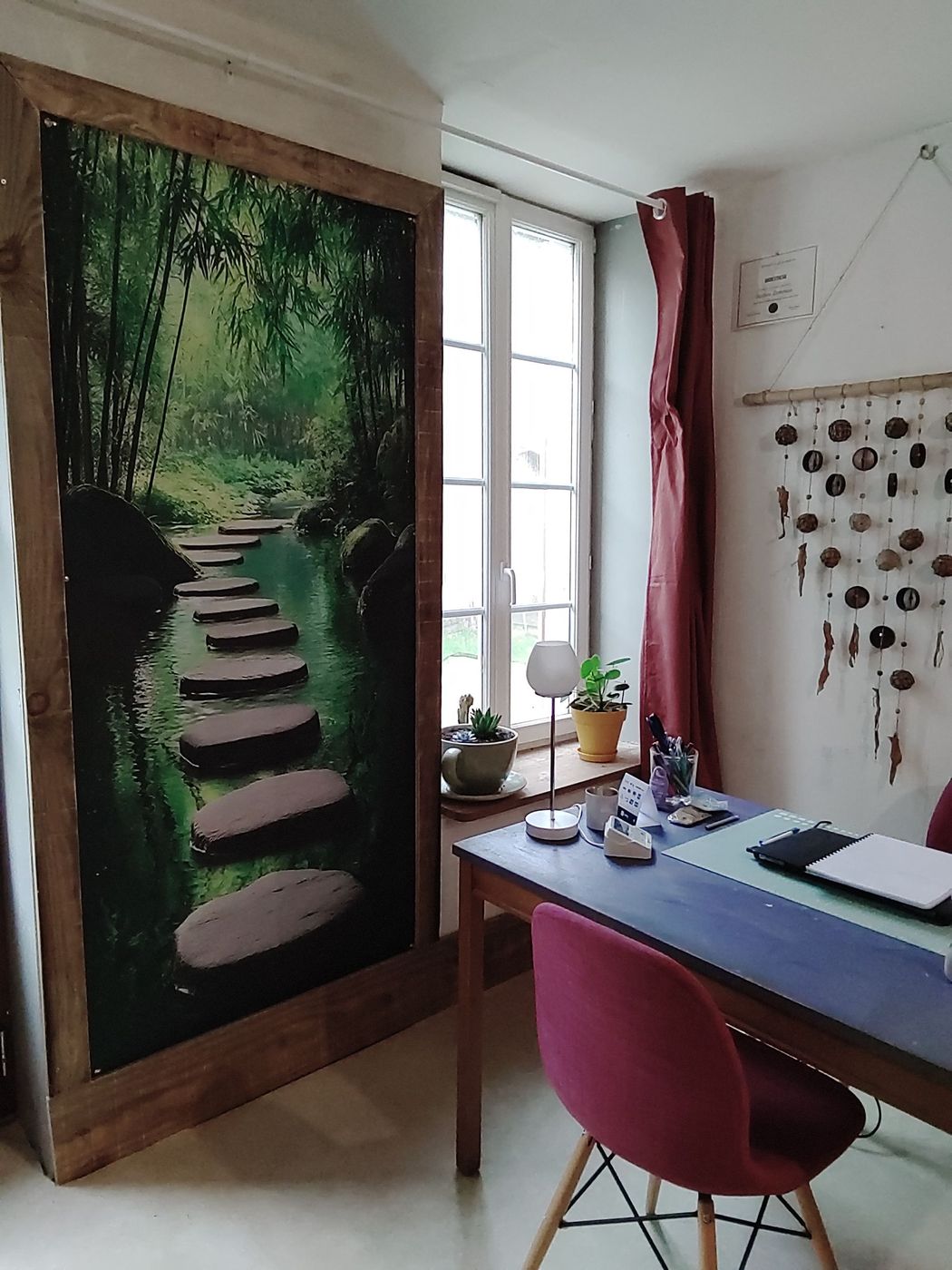 Bureau à domicile confortable avec porte murale, bureau près de la fenêtre, chaise rose et décoration murale suspendue.