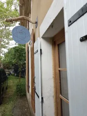 Bâtiment blanc avec une porte en bois et une enseigne bleue suspendue à une branche