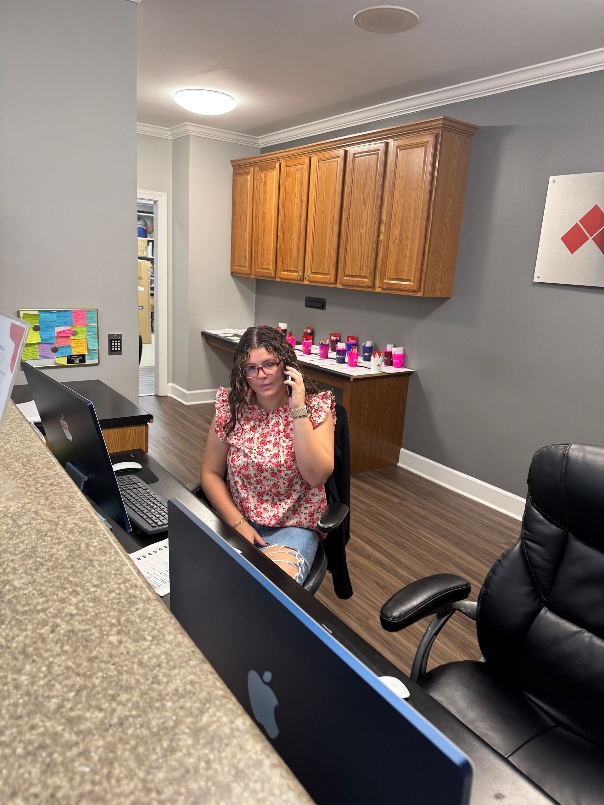 A woman is sitting at a desk talking on a cell phone.