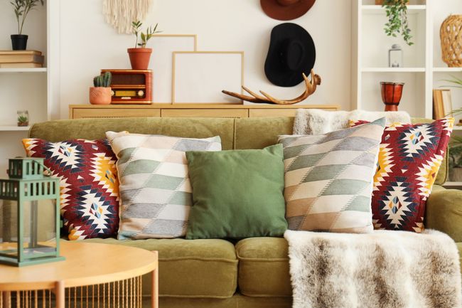 Cozy living room with olive sofa, patterned pillows, gold accents, and wall decor on a white shelf backdrop