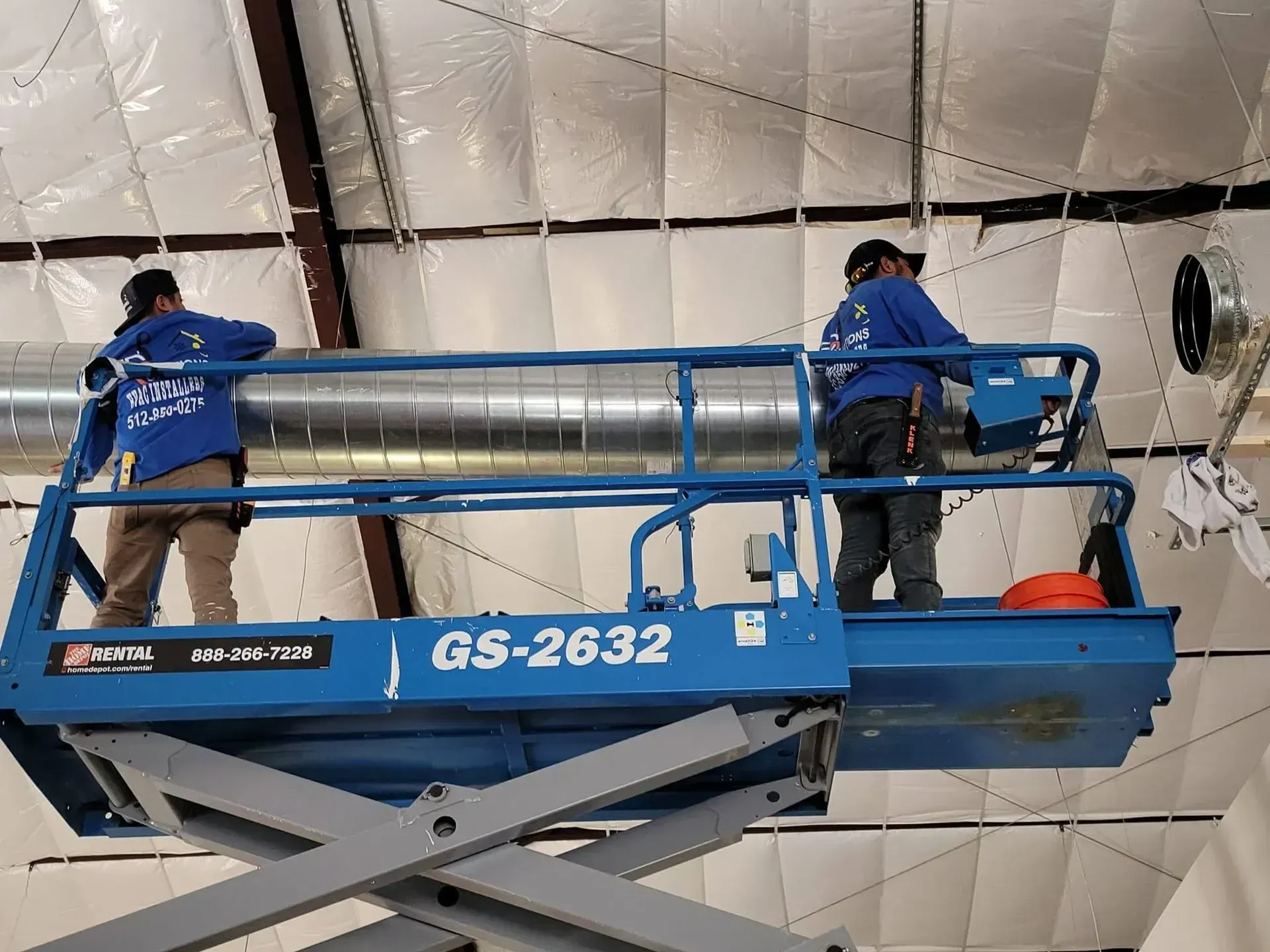 Workers in blue uniforms on a scissor lift inspecting a white insulated ceiling