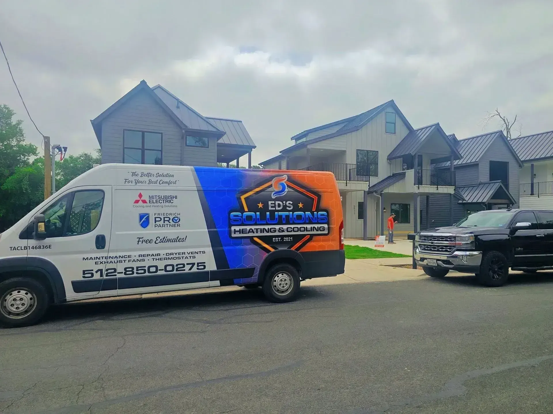Moving truck with company graphics parked on a residential street beside modern houses.