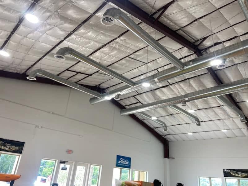 Warehouse interior with high metal ceiling, exposed ductwork, white walls, and windows near the entrance