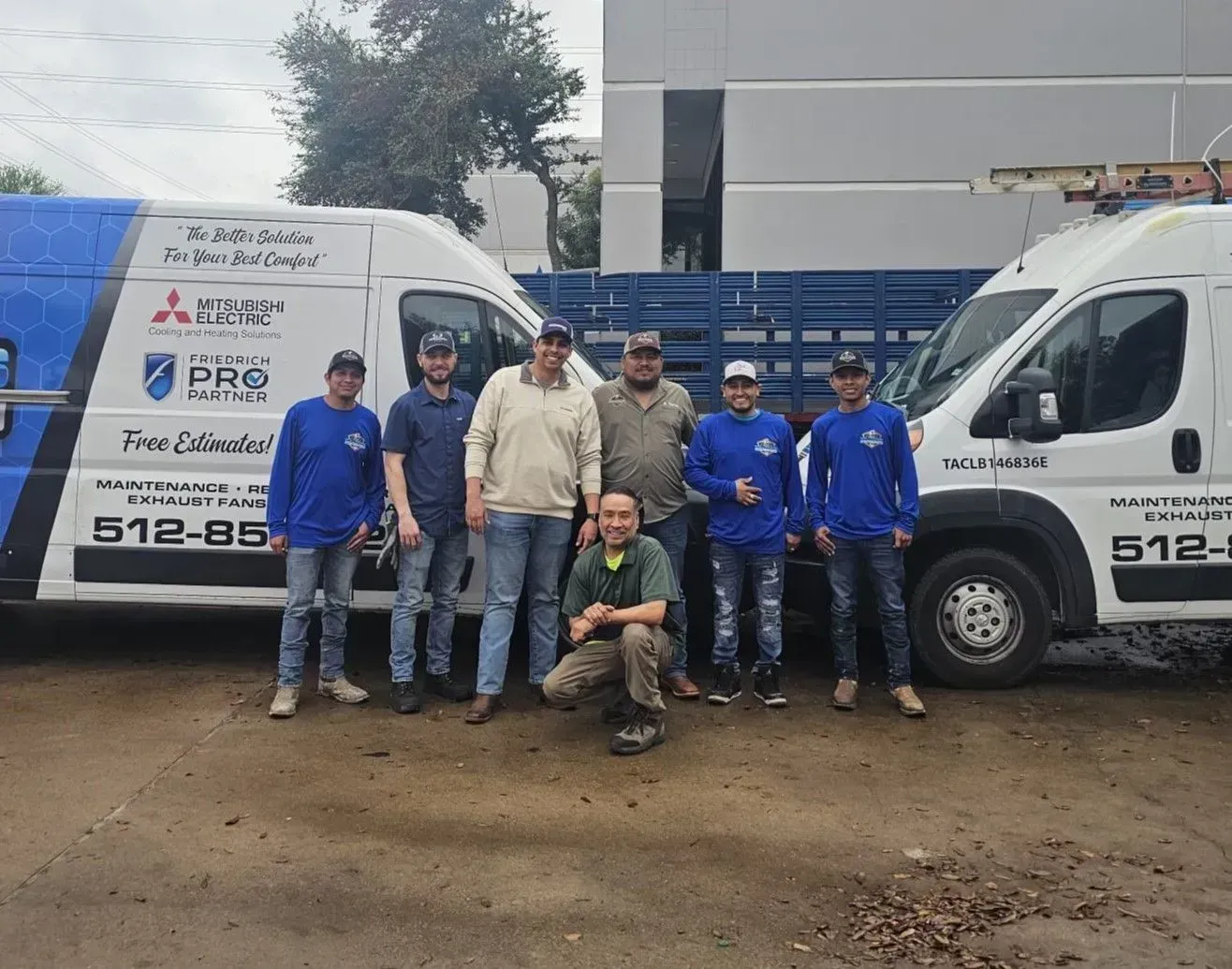 Seven workers posing beside white company vans at a muddy job site.