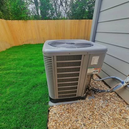 Outdoor HVAC unit beside a house, with green lawn, gravel, and wooden fence in the background