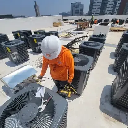 Worker in orange safety gear and white hard hat inspecting rooftop HVAC units.